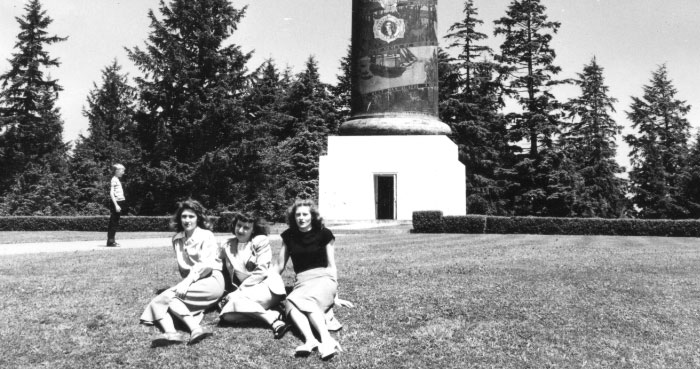 Three girls sit at the base of the Astoria Column in the 1940s